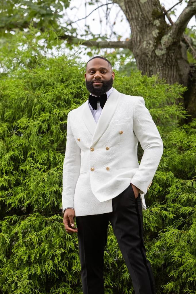 Man in a white Double Breasted Tuxedo with gold buttons standing in a green outdoor setting