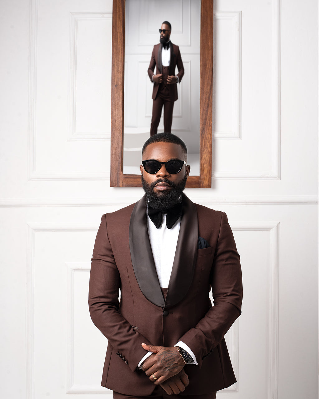 Man in a brown Tuxedo with a mirror reflection on a white paneled wall
