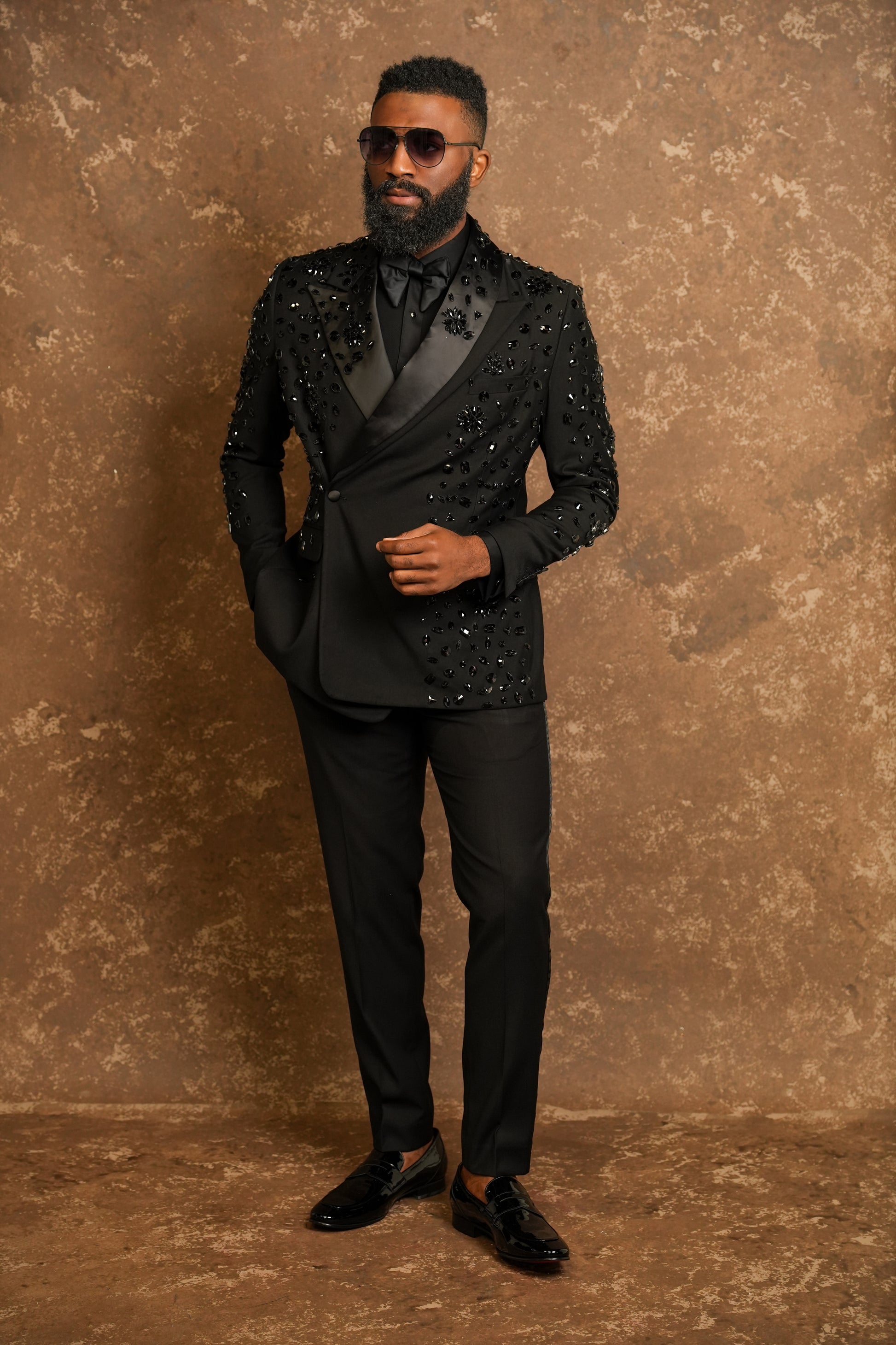 Man wearing a black tuxedo with sequin details against a brown textured background