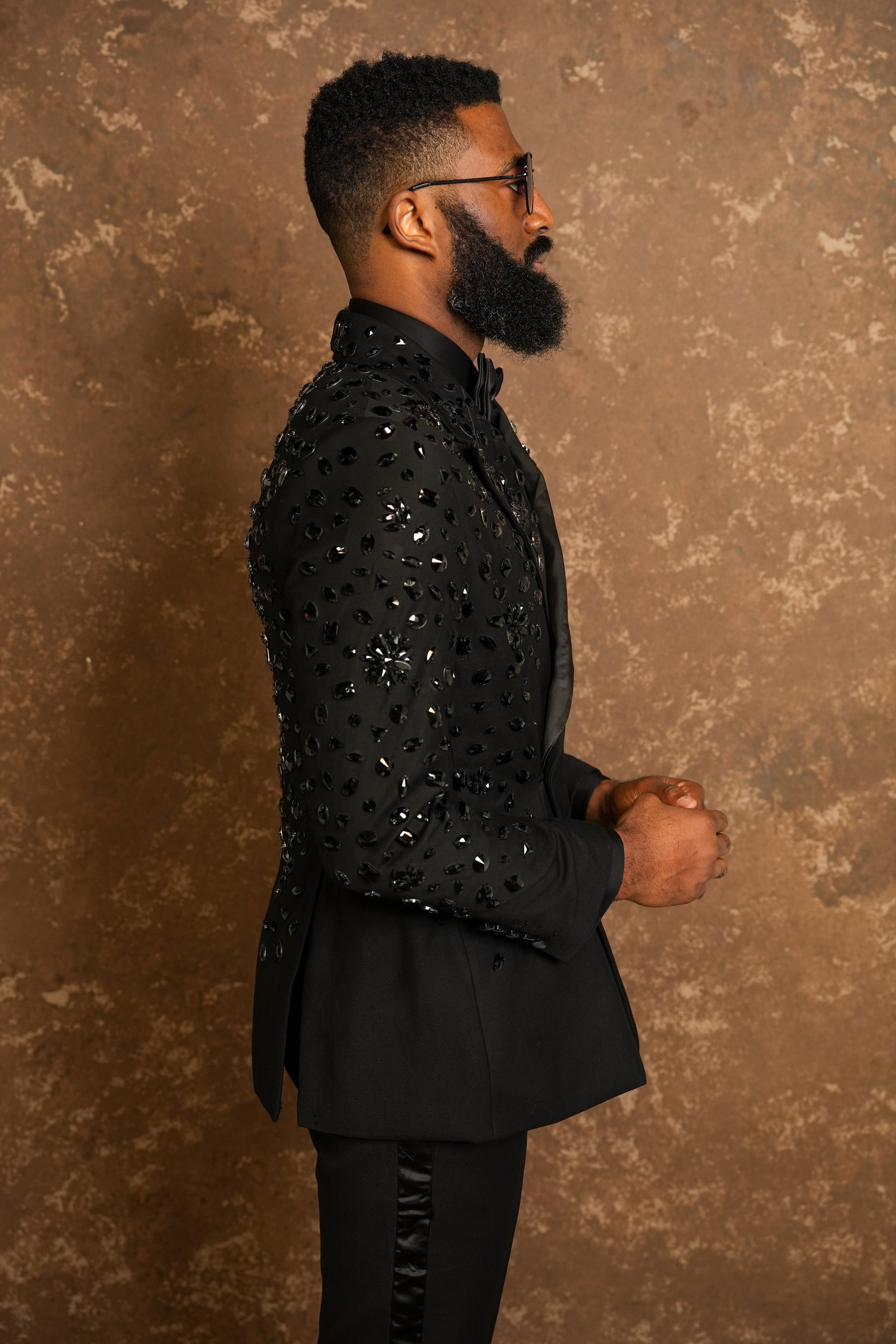 Man wearing a black sequin tuxedo against a brown textured background