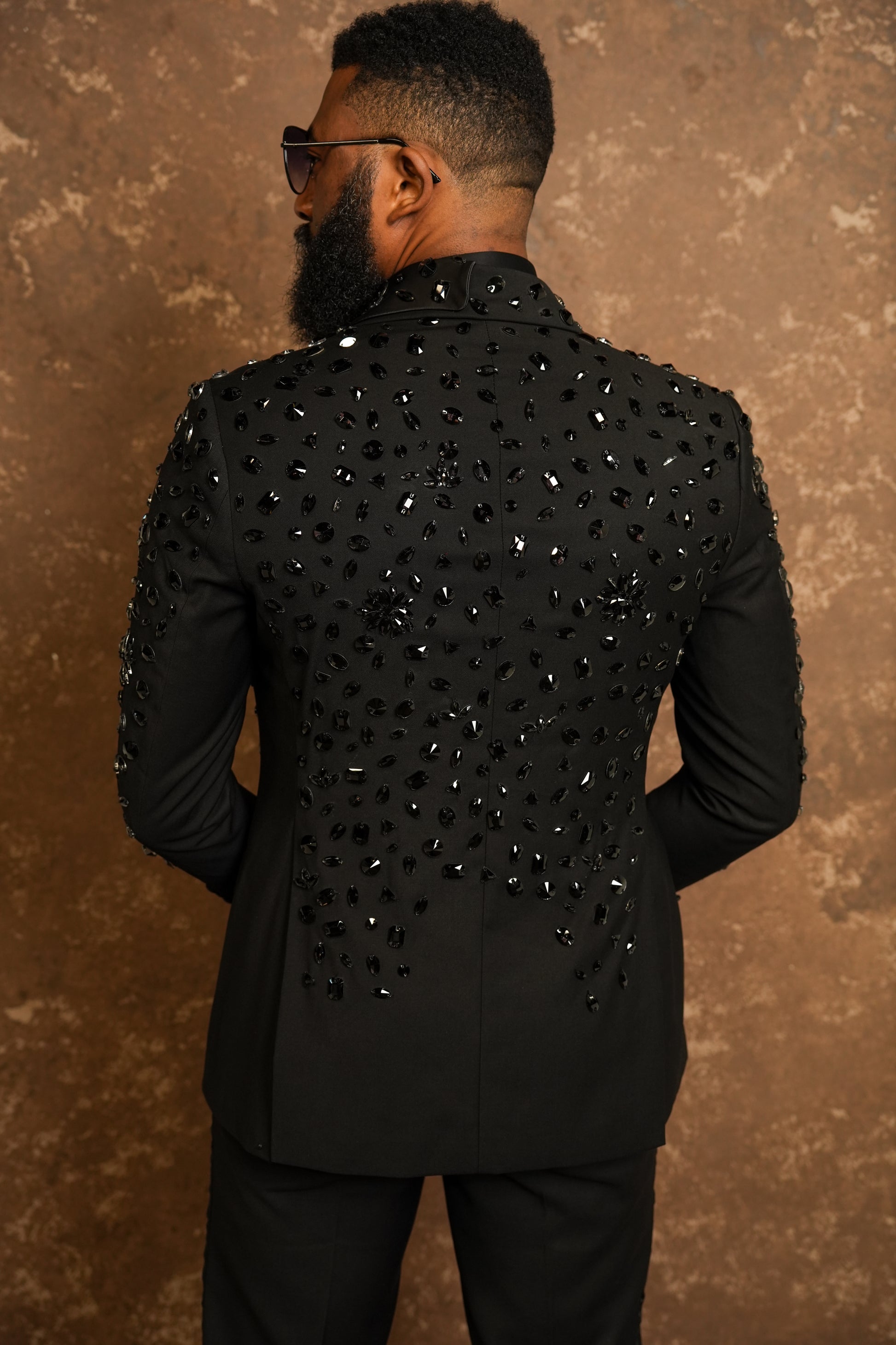 Man wearing a black tuxedo with sequin details against a brown background