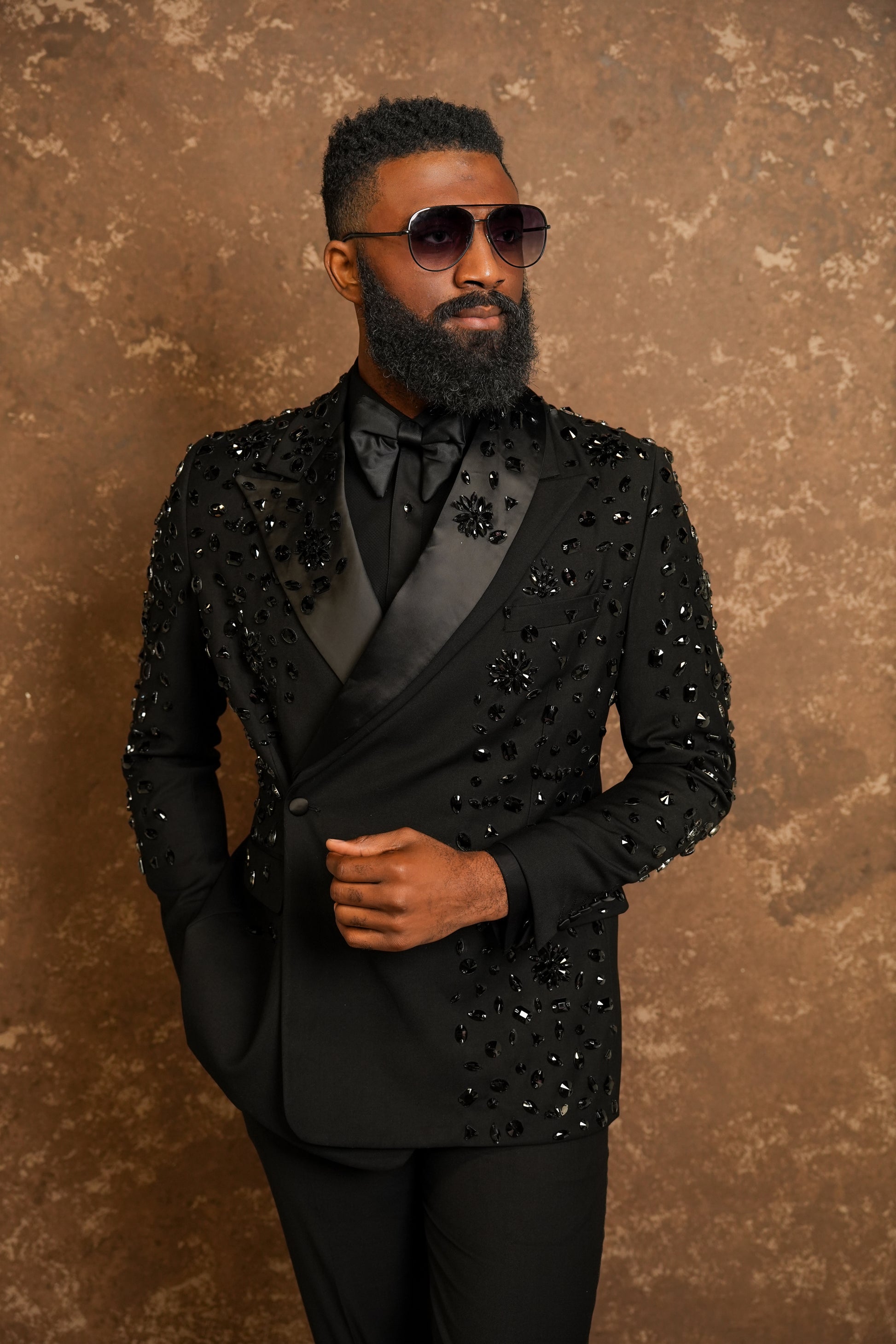 Man wearing a black suit with embellishments against a brown background