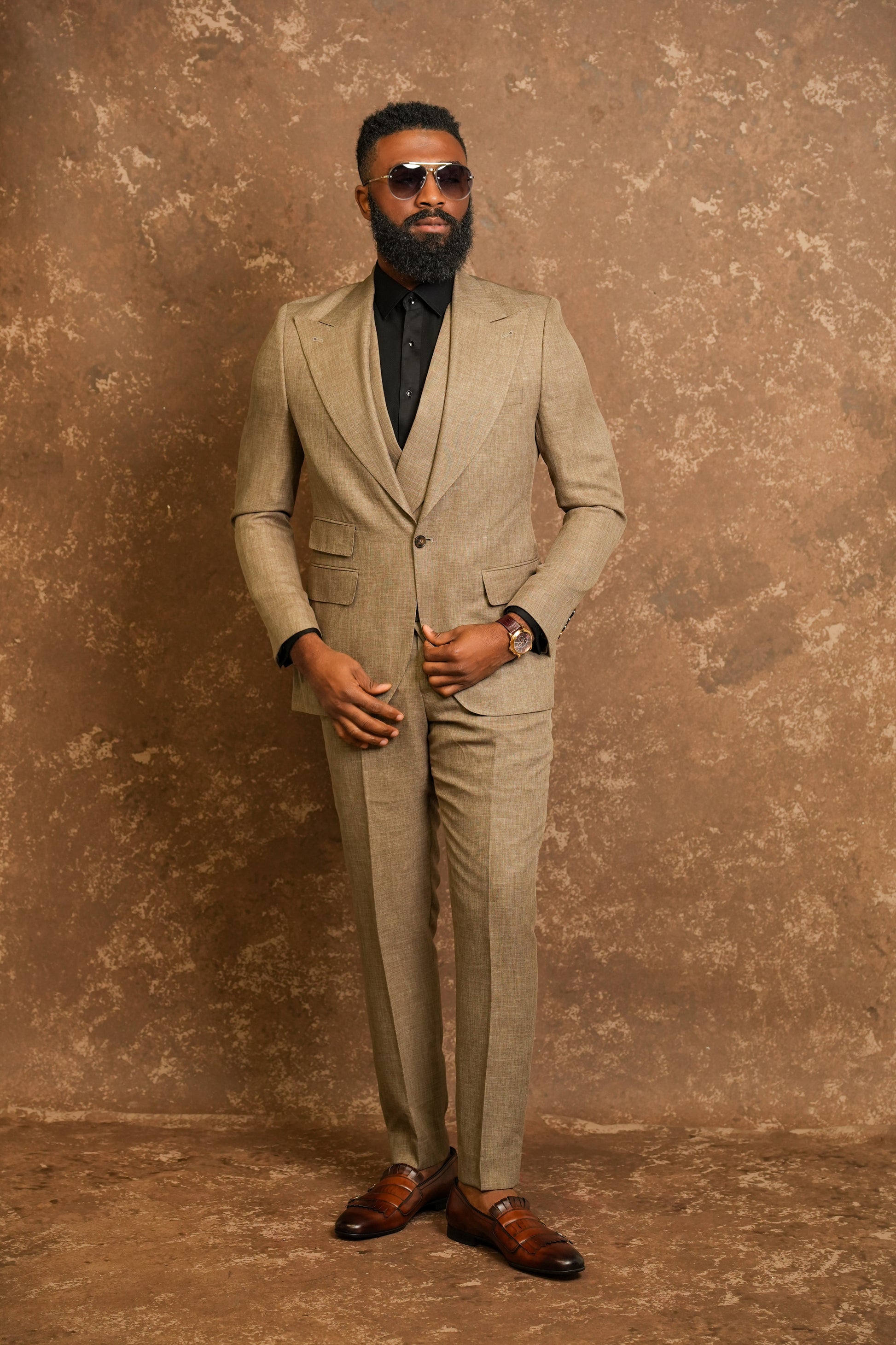 Man wearing a beige suit and sunglasses against a textured brown background