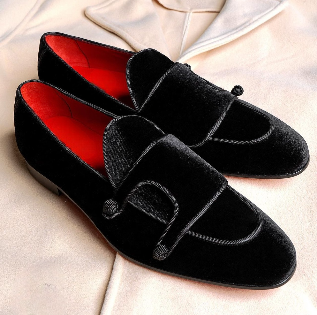 Black velvet loafers with red interior on a light beige background