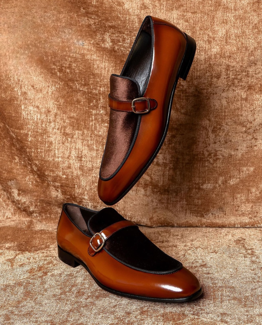 Pair of brown and black leather shoes with a buckle on a textured brown background
