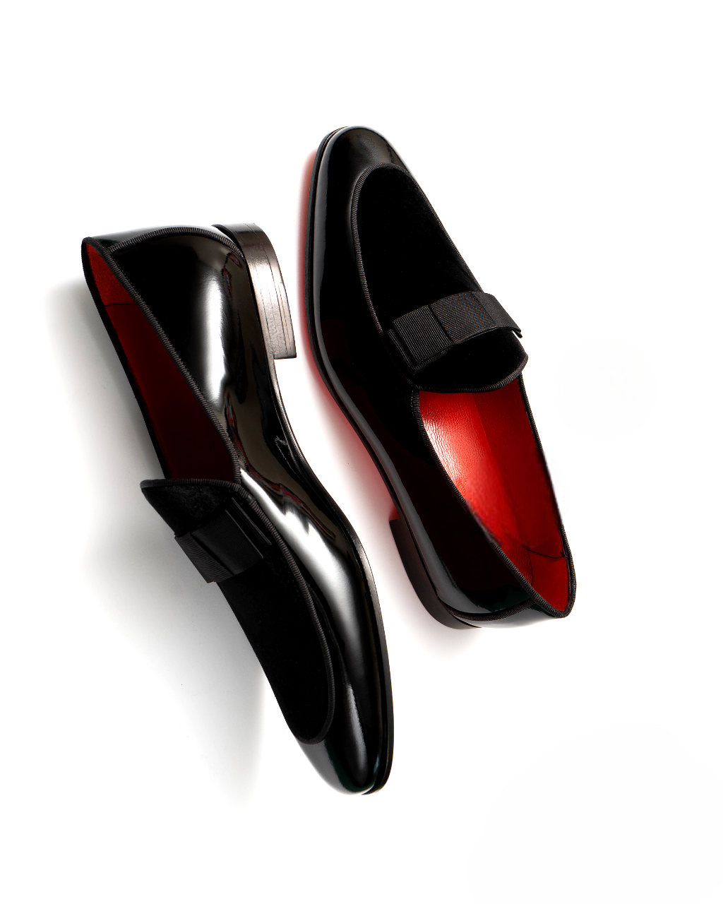 Black loafers with red soles on a white background