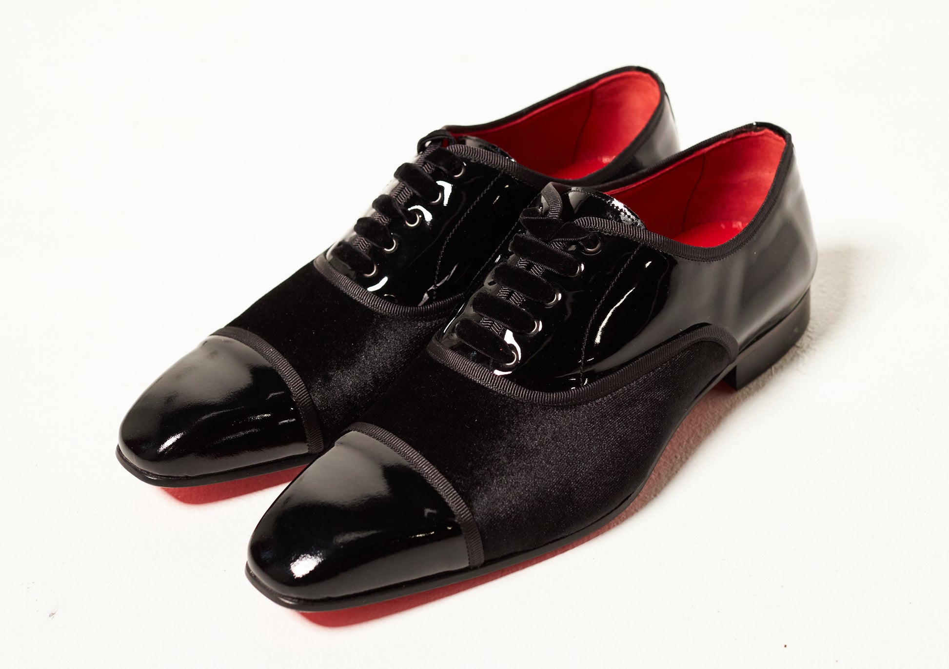 Black dress shoes with red soles on a white background