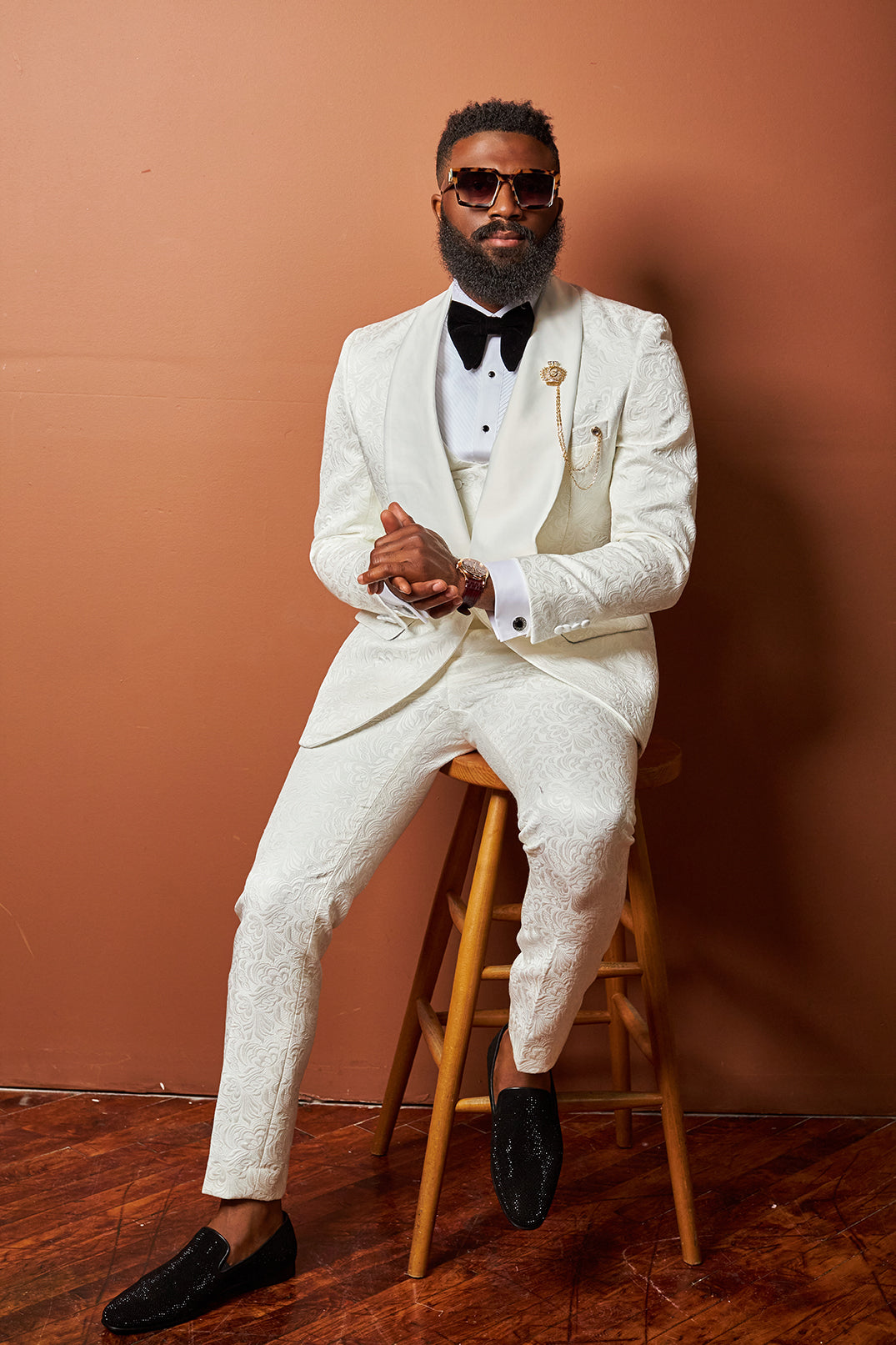 This image shows a custom ivory tuxedo featuring a paisley brocade pattern and a black bow tie