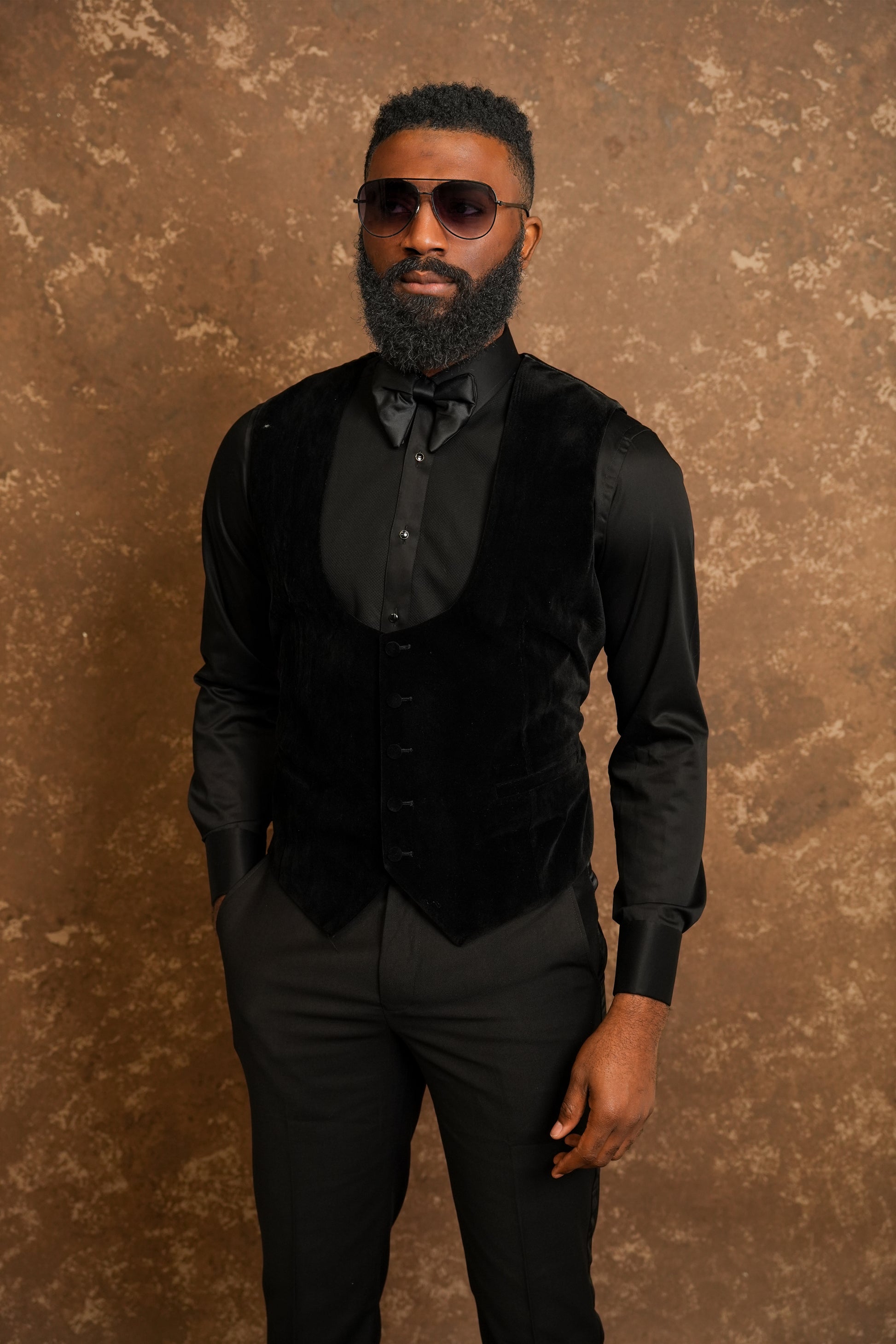 Man in a Black Tuxedo standing against a textured brown background