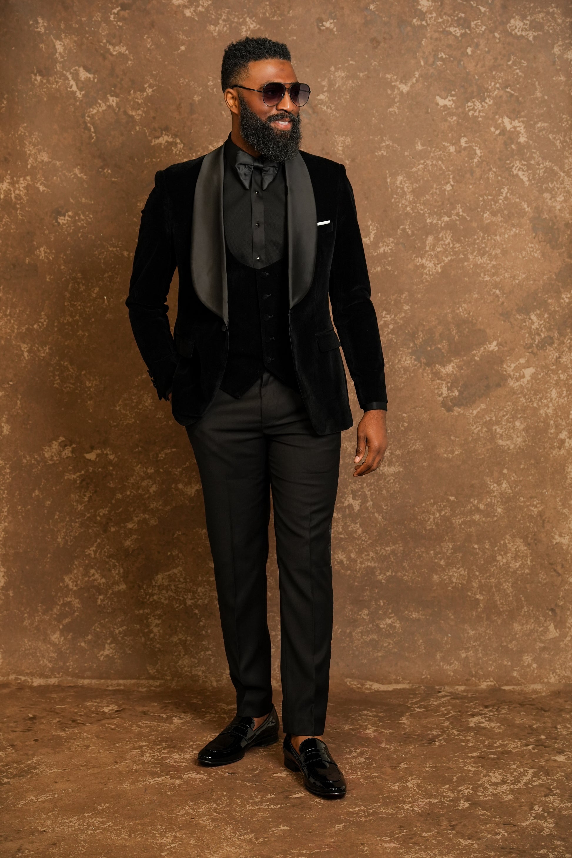 Man in a Black Tuxedo standing against a textured brown background